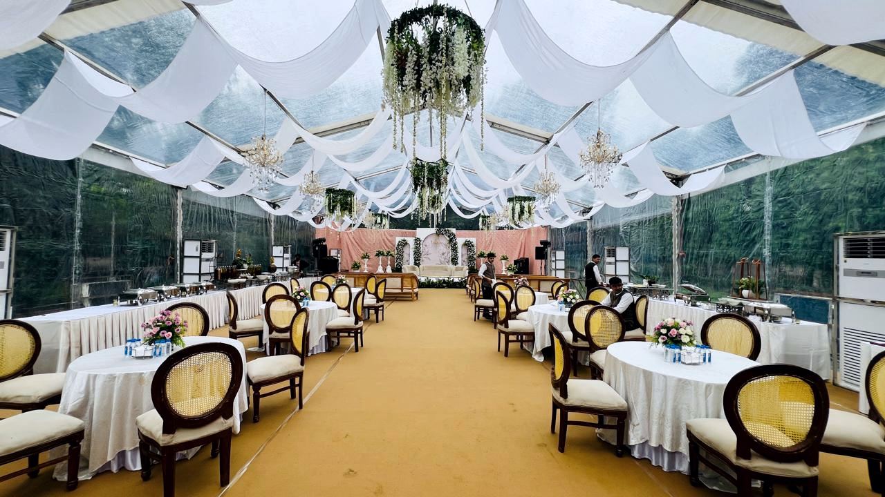 Dinner tables under white drapes in a transparent hangar, a tower AC along the glazing