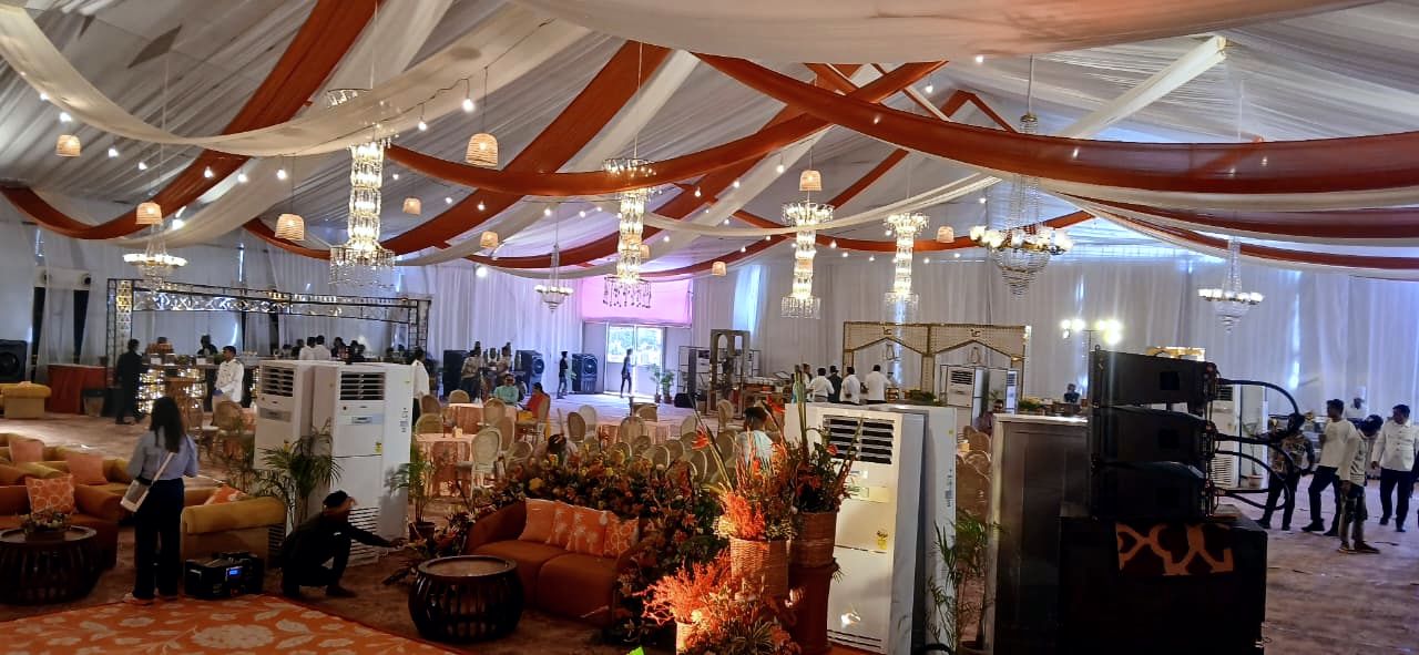Wedding hall under orange and cream drapes with tower ACs placed between the décor